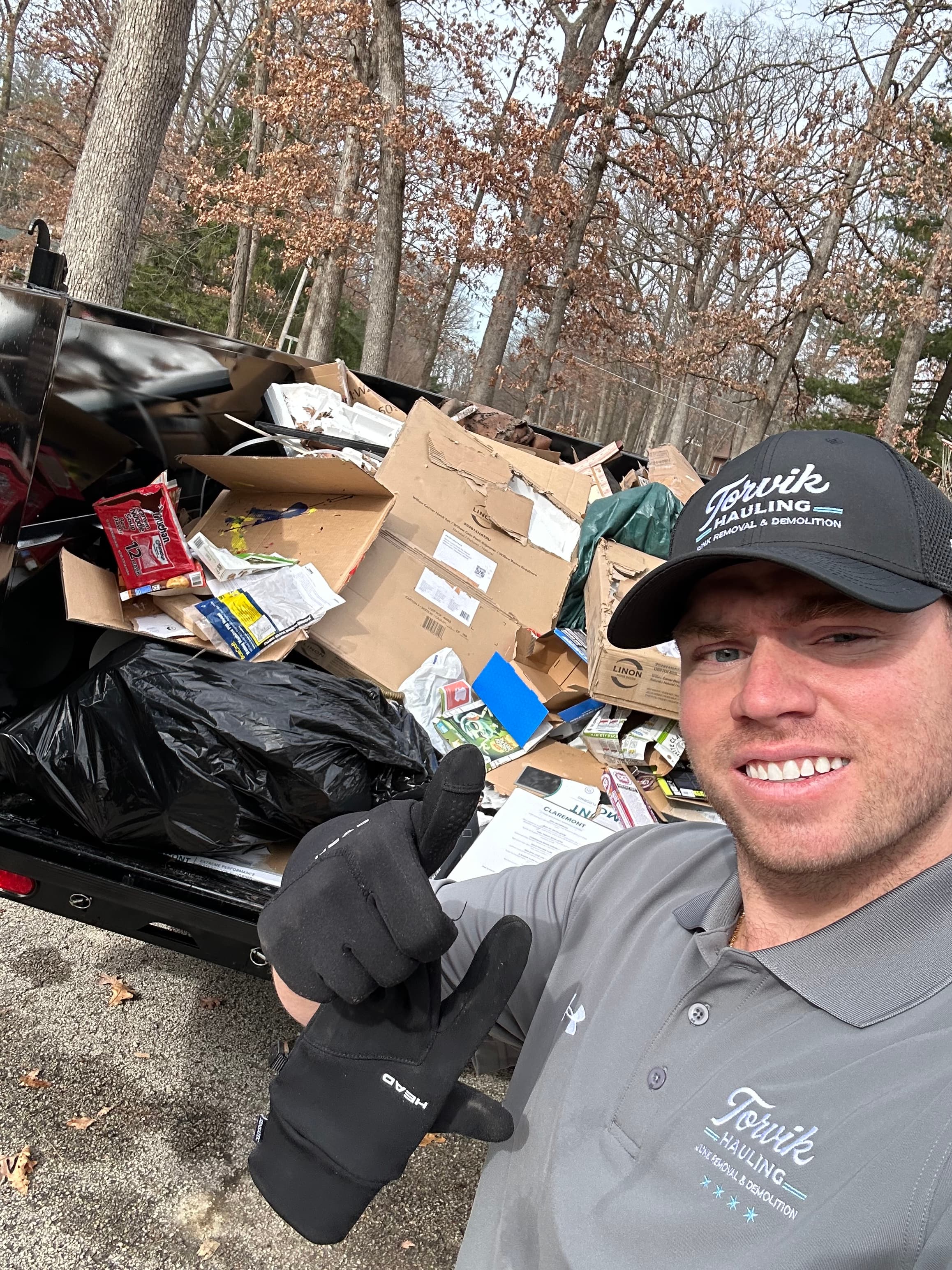Torvik Hauling owner giving a thumbs-up next to a trailer loaded with boxes, bags, and household junk mid-haul