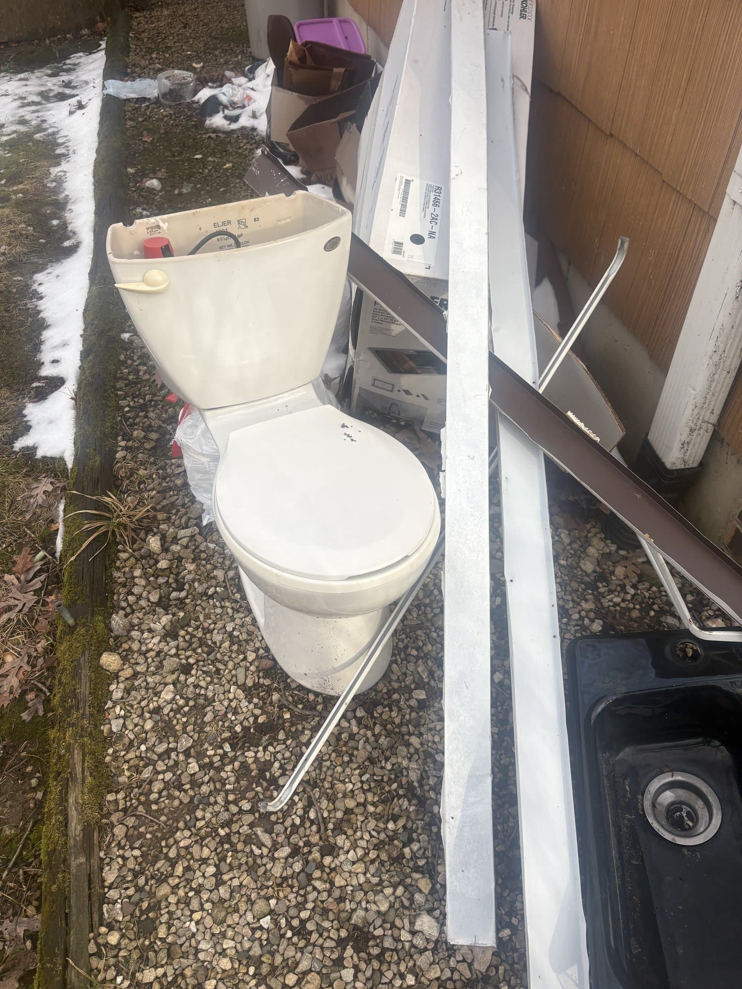 Old toilet and construction debris piled against the side of a house