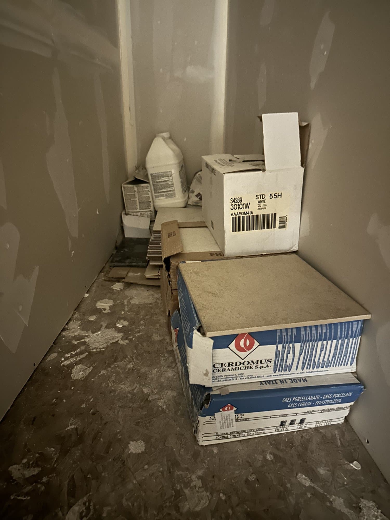 Construction tile boxes, packaging, and renovation debris stacked in a small drywalled room