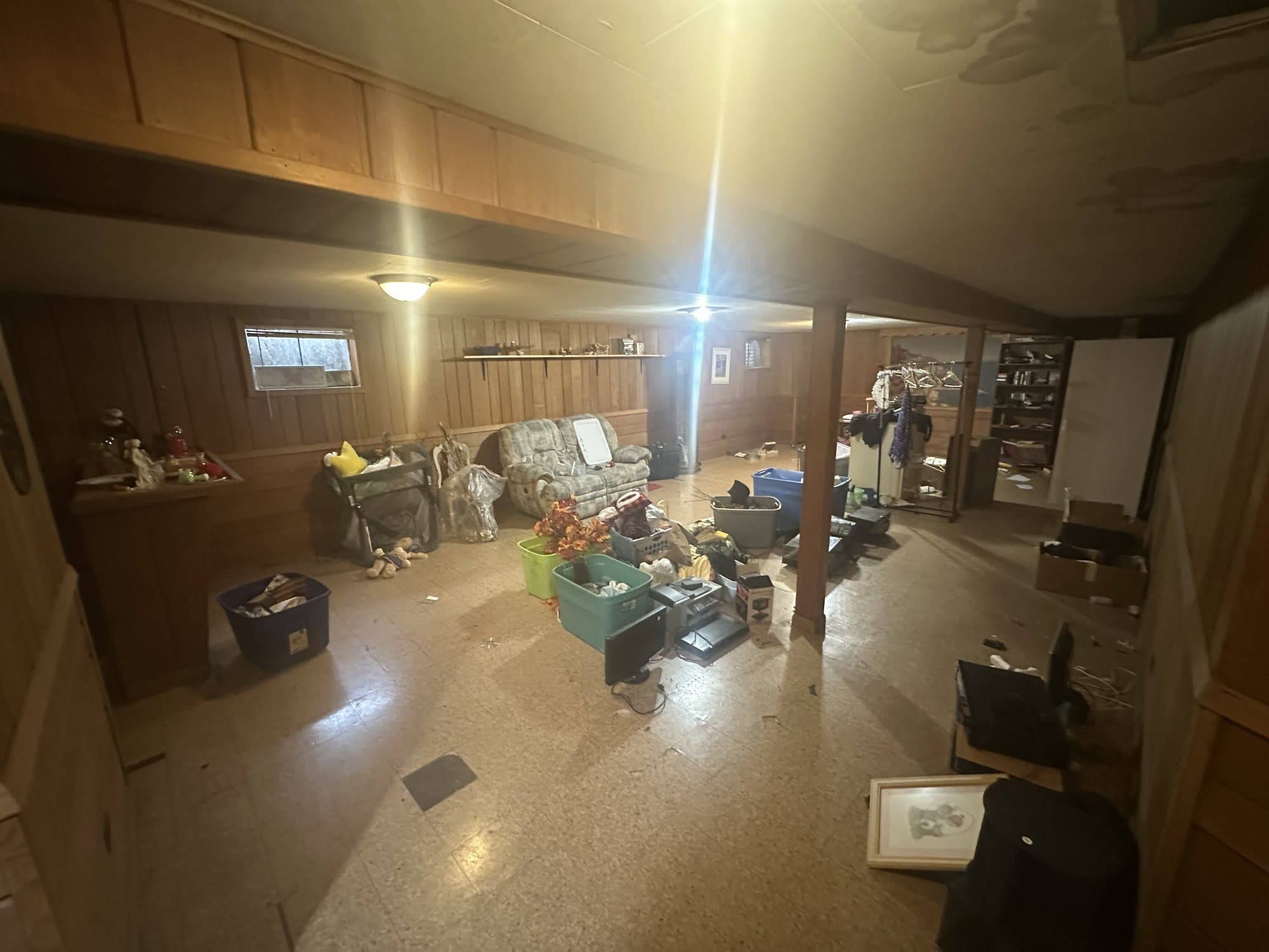Cluttered basement living area with sofa, totes, and household items