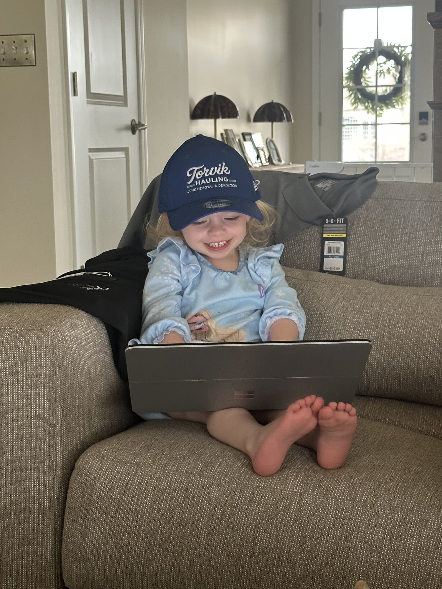 The owner's young daughter wearing a Torvik Hauling cap, smiling on the family couch — family-owned and community-focused