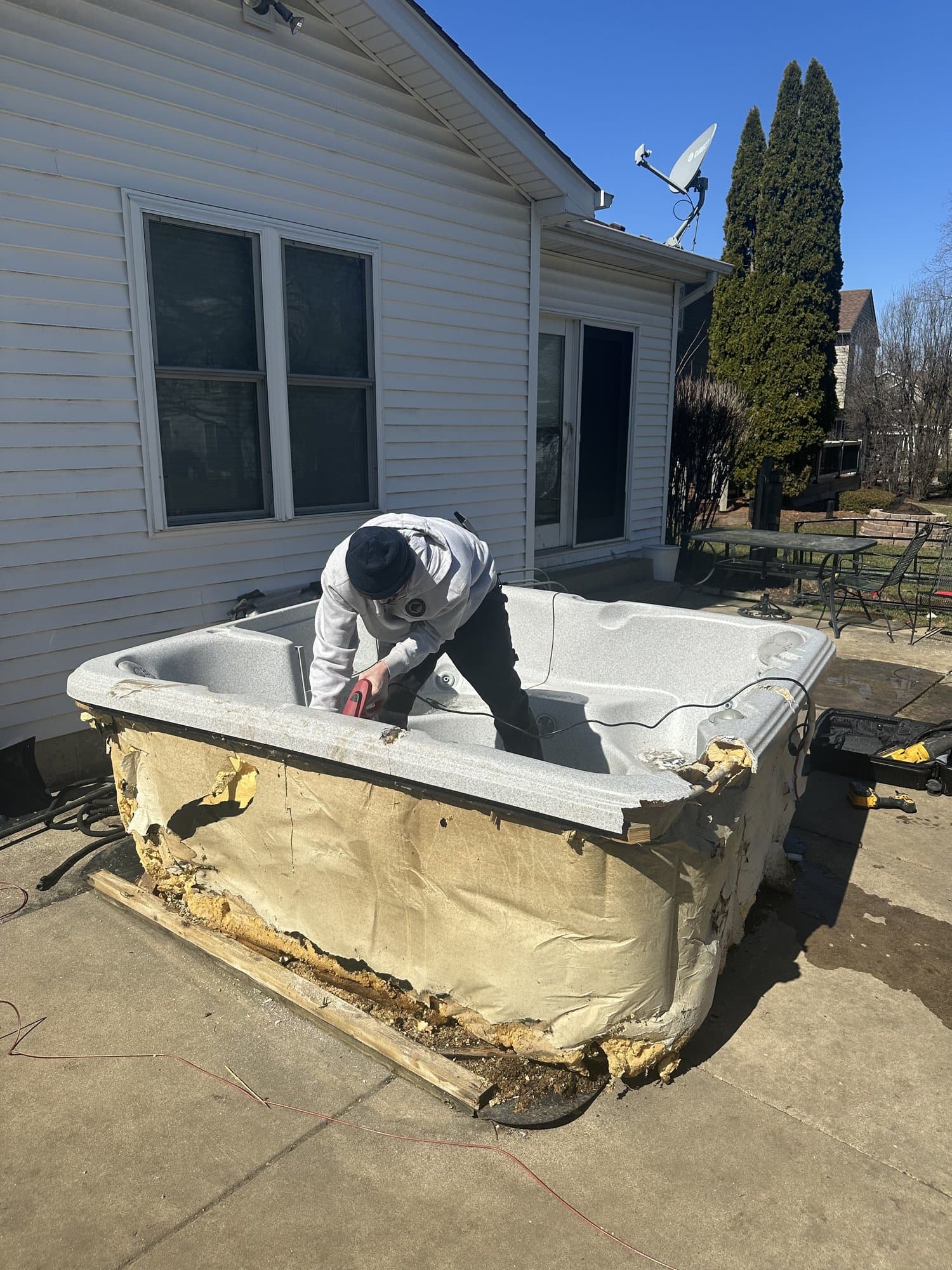 Torvik Hauling crew member breaking down a worn-out hot tub on a suburban patio during a cleanout